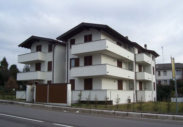 A multi-story residential building with balconies, a gated entrance, and a small garden area.