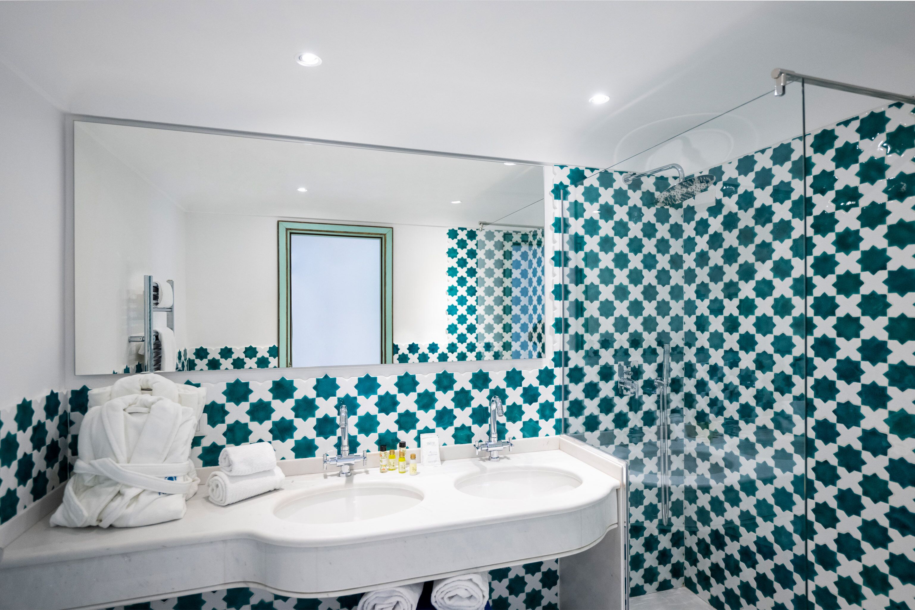 A bathroom with two sinks, a large mirror, and a shower with a geometric tile pattern.