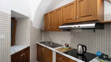 A kitchen with wooden cabinets, a stainless steel sink, a marble countertop, and a kettle.