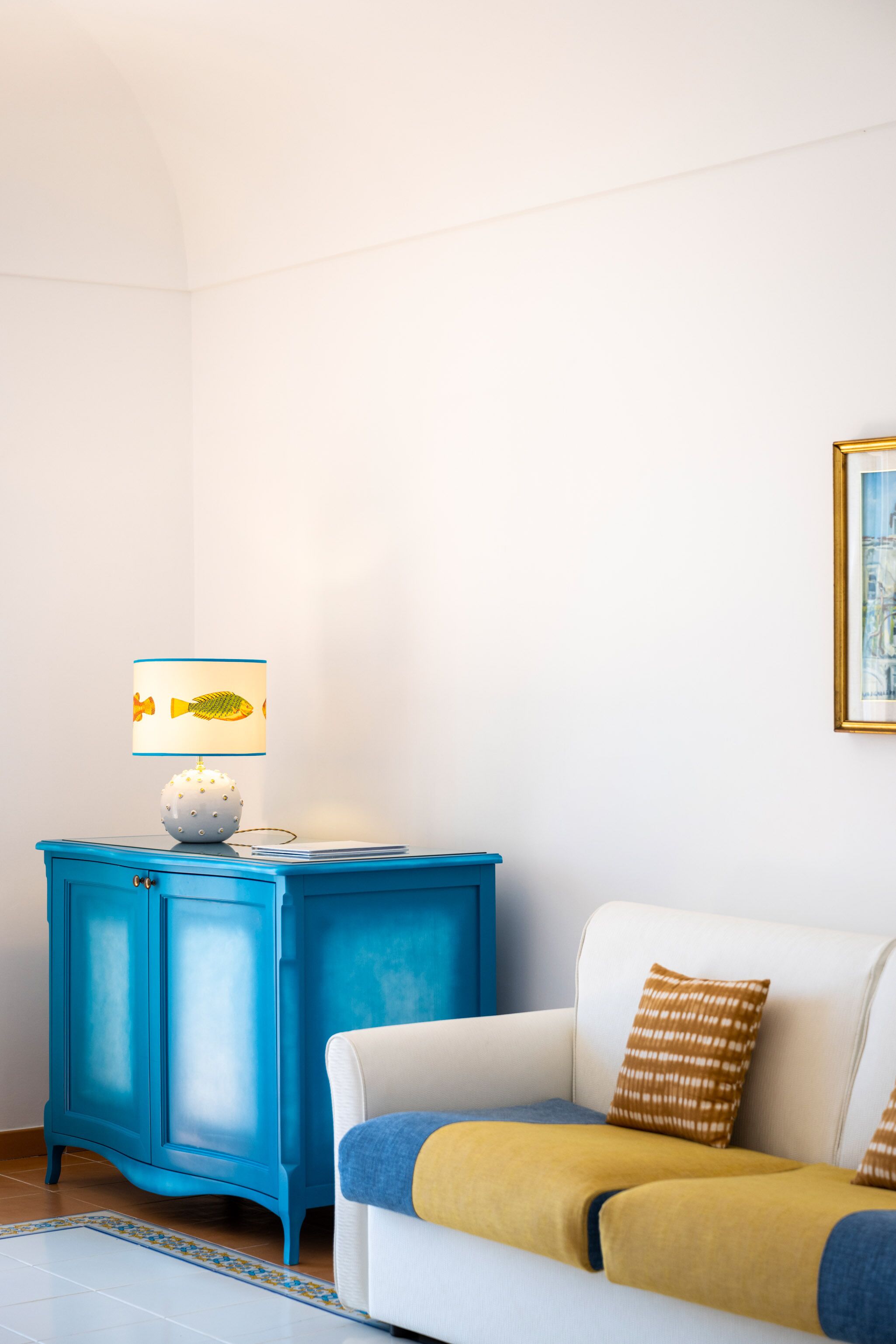 A room with a white sofa, a blue cabinet, and a lamp with a fish design.