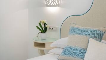 A neatly made bed with patterned pillows, a bedside table with a potted plant, and a wall-mounted light fixture.