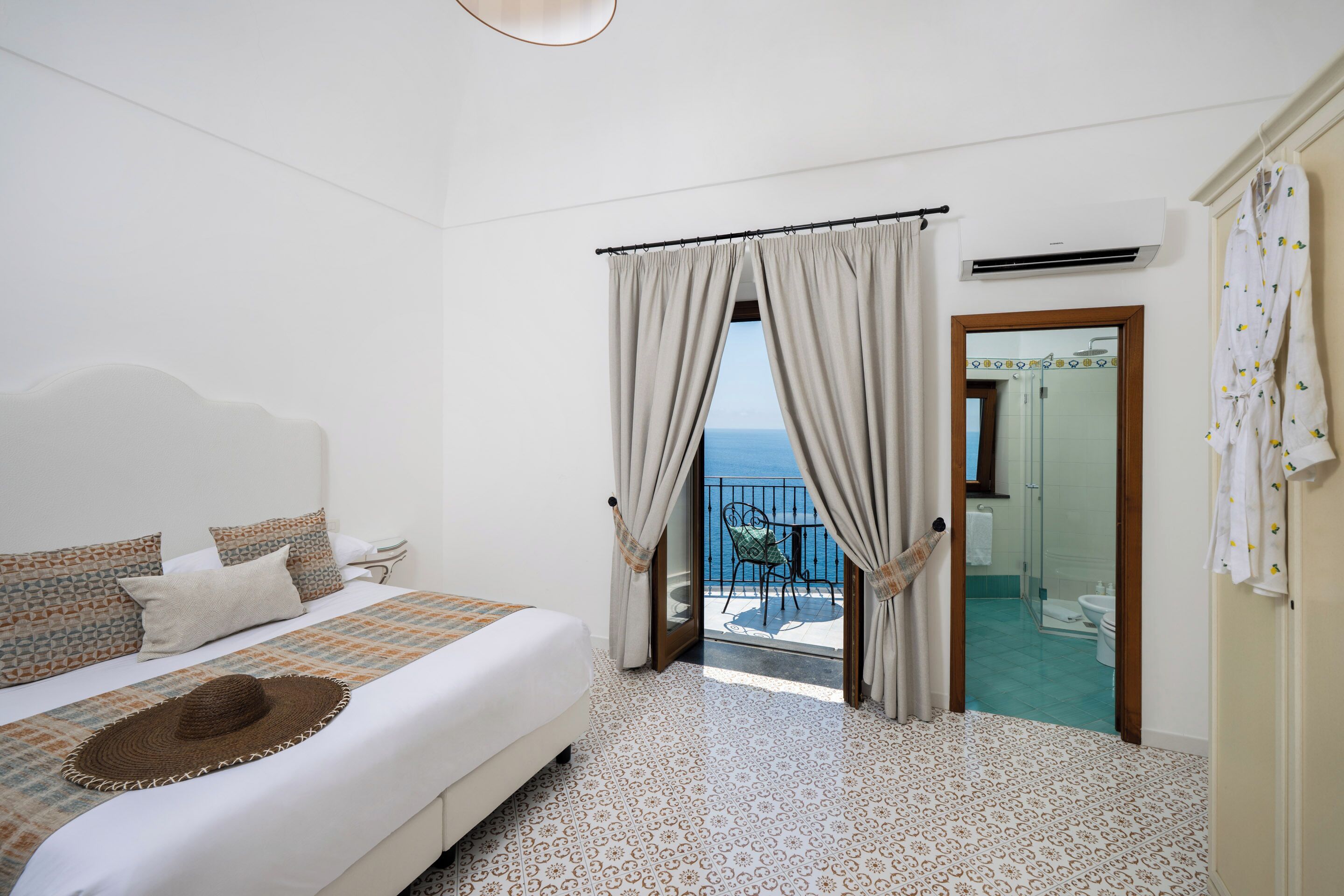 Habitación de hotel con cama, vistas al mar, baño con ducha y balcón con una silla.