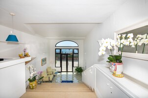Una escalera conduce a una puerta con vistas al exterior. Hay plantas en macetas y una lámpara azul a la izquierda.