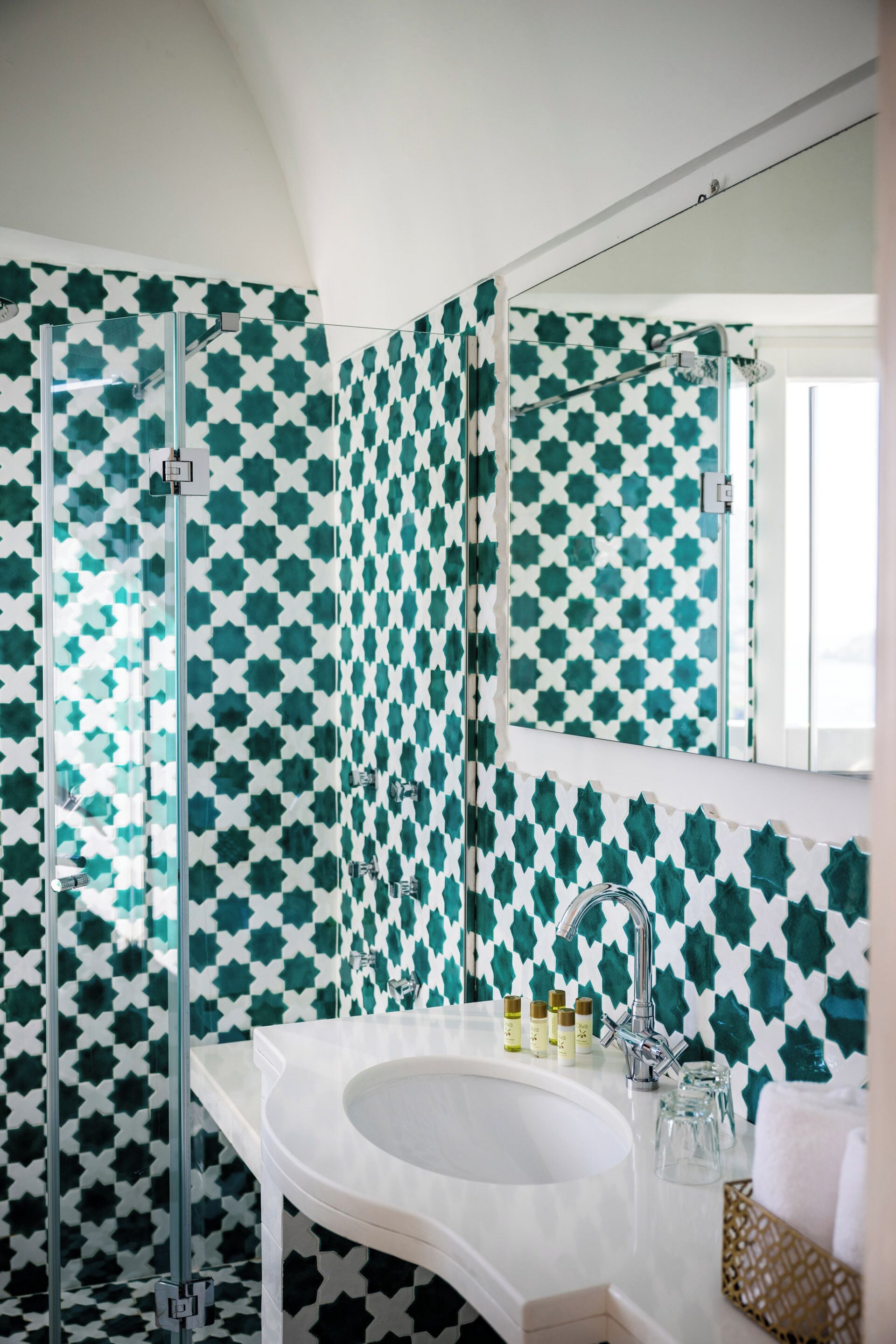A bathroom with a white sink, a glass shower enclosure, and a patterned wall.