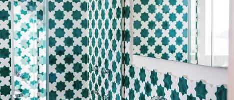 A bathroom with a white sink, a glass shower enclosure, and a patterned wall.