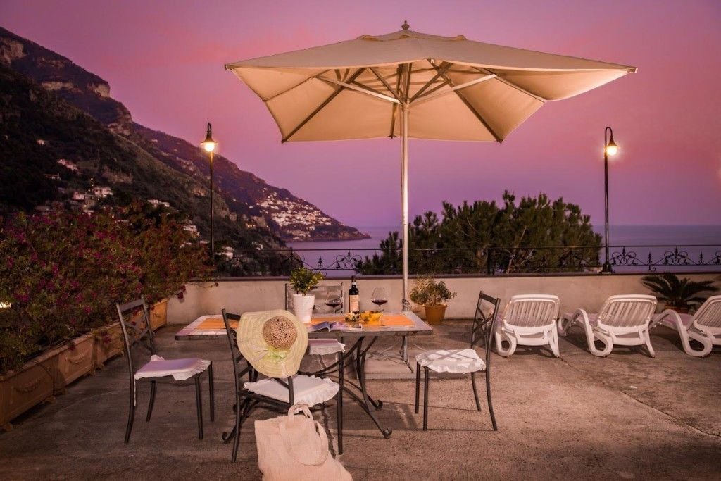 An outdoor patio with a table, chairs, and an umbrella, overlooking a coastal landscape at dusk.