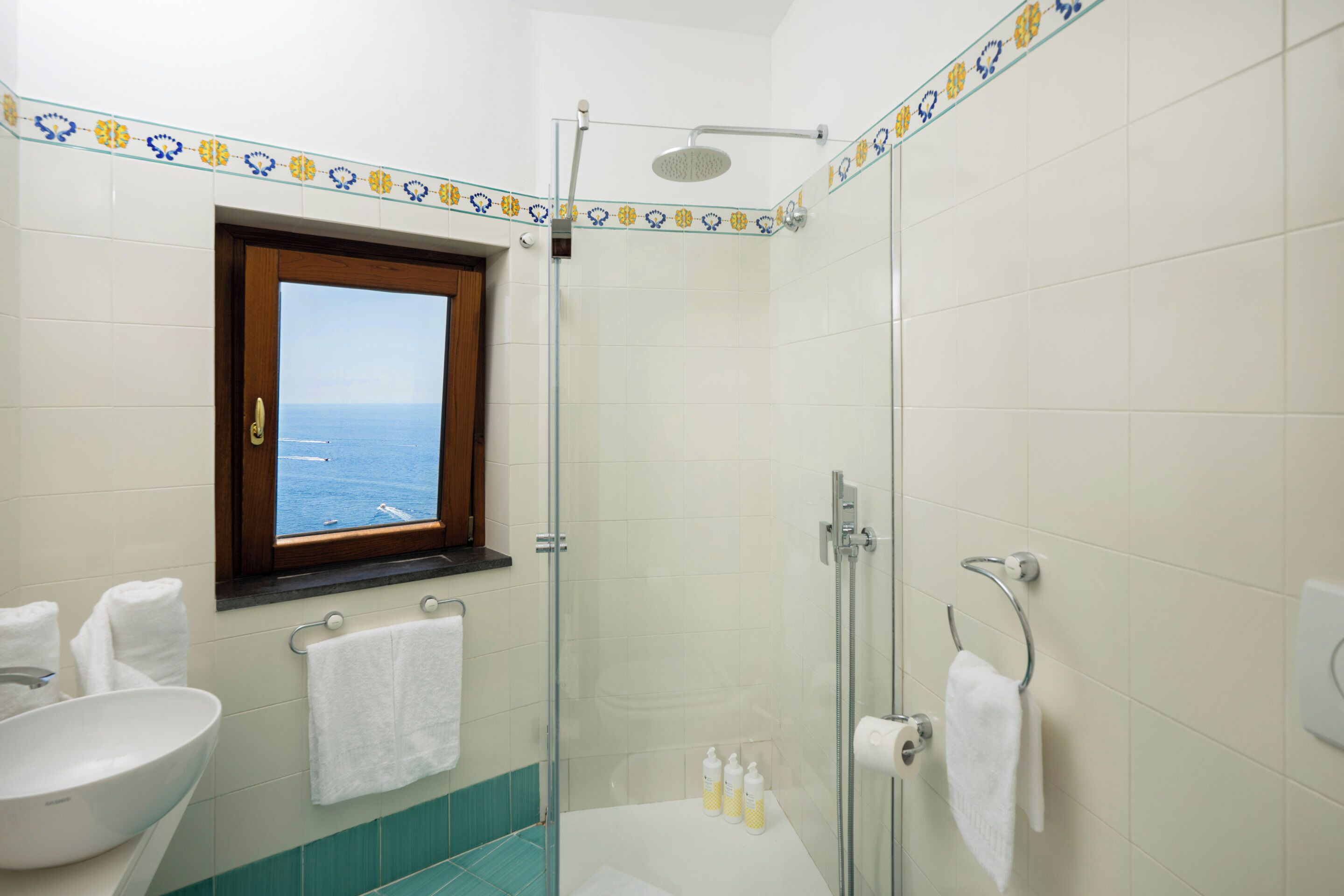 Un baño con ducha, lavamanos y ventana con vista al mar.