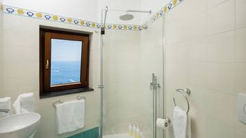 Un baño con ducha, lavamanos y ventana con vista al mar.
