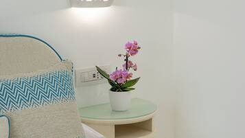 A neatly arranged bedroom with a bed, pillows, a bedside table with a potted orchid, and a wall-mounted light fixture.