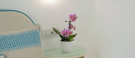 A neatly arranged bedroom with a bed, pillows, a bedside table with a potted orchid, and a wall-mounted light fixture.