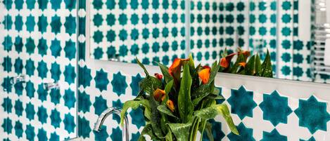 A bathroom with a sink, two faucets, a mirror, and a potted plant with flowers.
