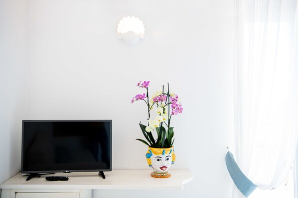 A TV on a white shelf with a colorful vase of flowers. - Alcione Residence (Positano)