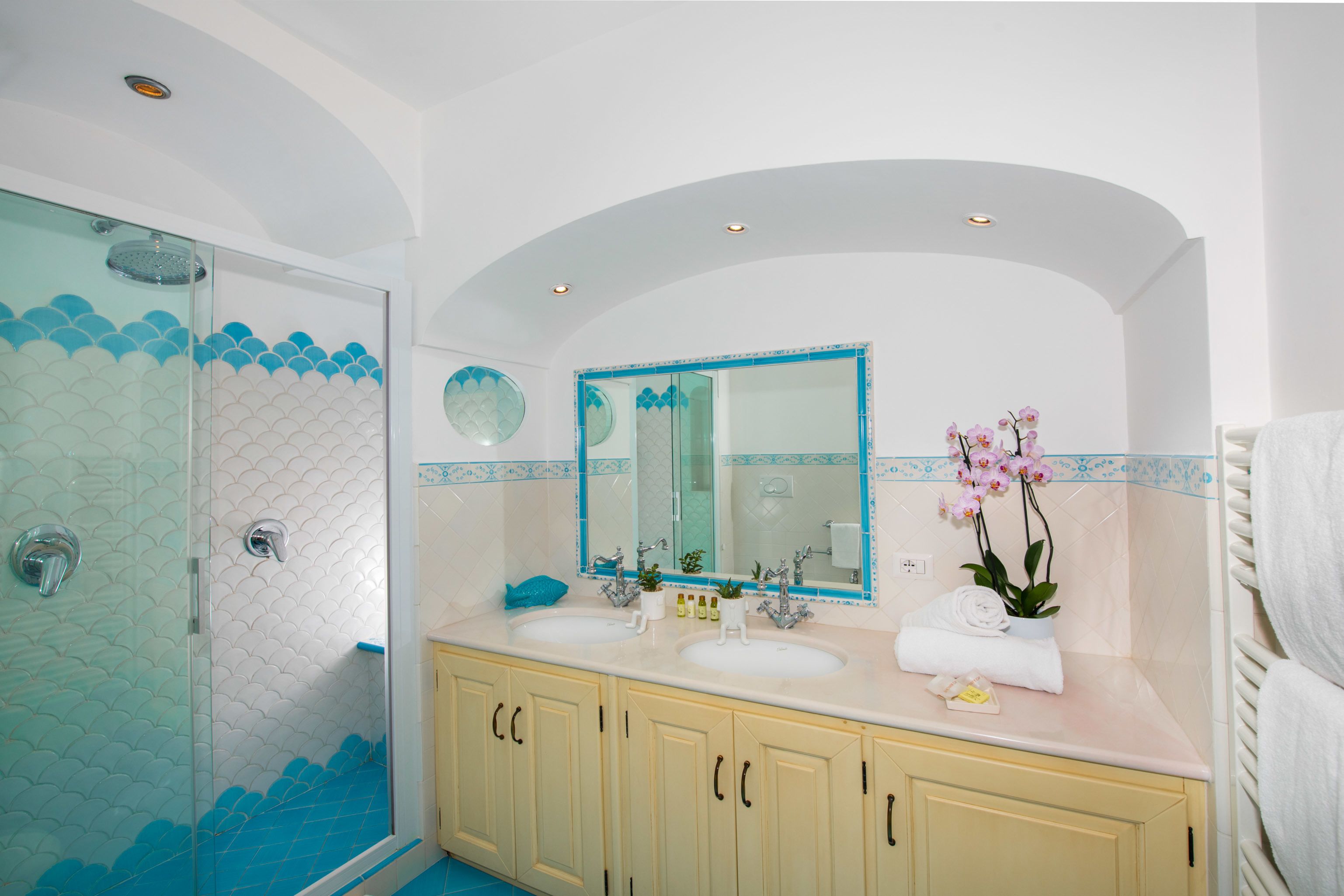 A bathroom with a glass-enclosed shower, two sinks, a large mirror, and a potted orchid.