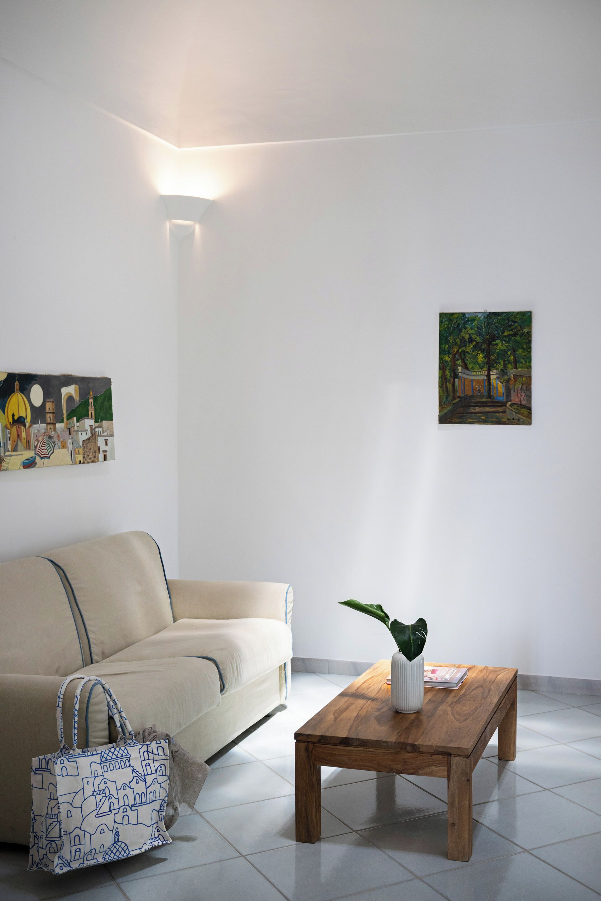 A living room with a sofa, a coffee table with a plant, a painting on the wall, and a lamp.
