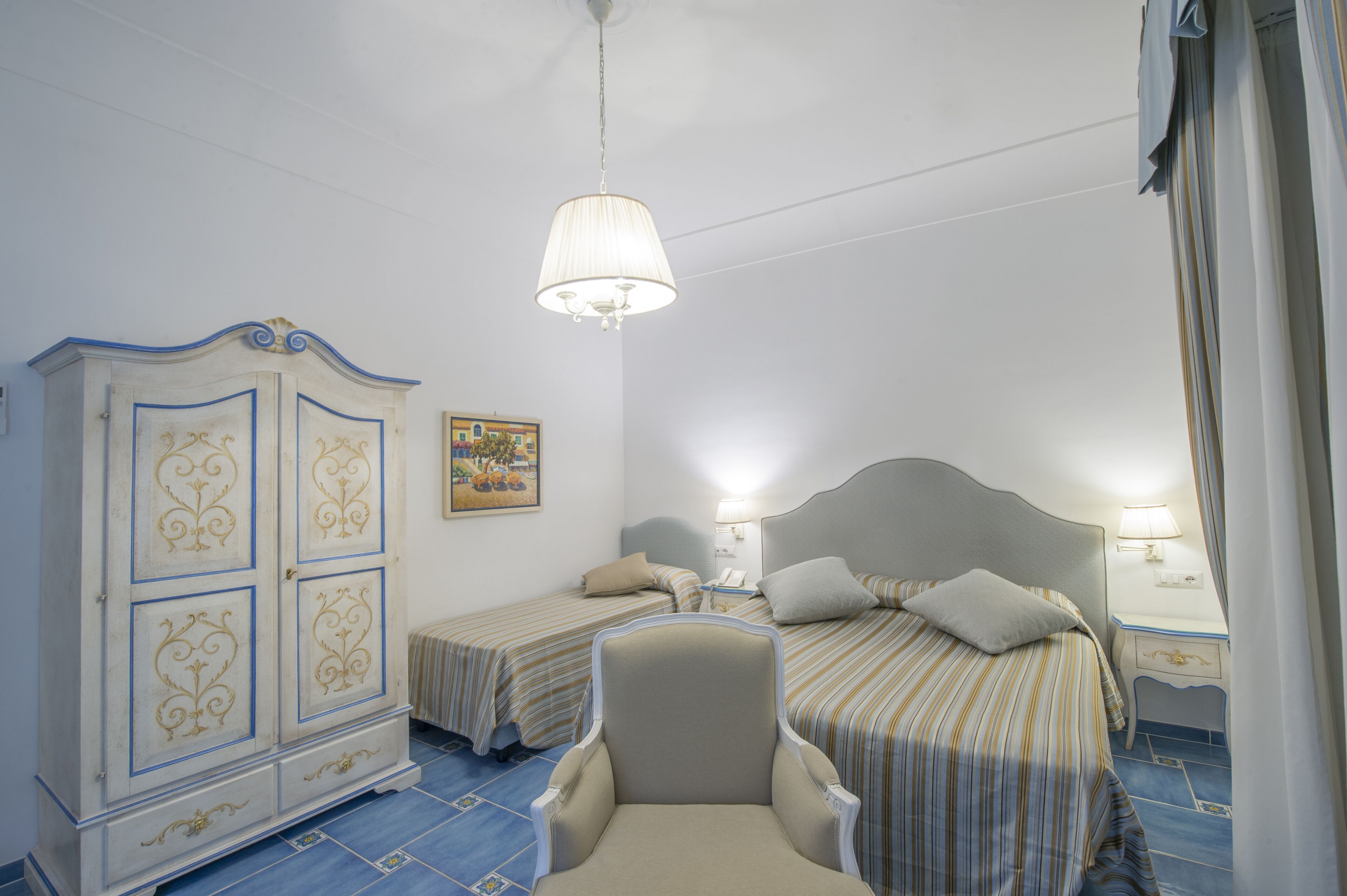 Una habitación de hotel con dos camas, un armario, una silla y un cuadro en la pared.