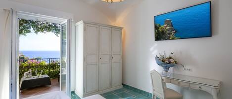 A bedroom with a bed, a desk, a chair, a wardrobe, and a painting of a coastal scene.