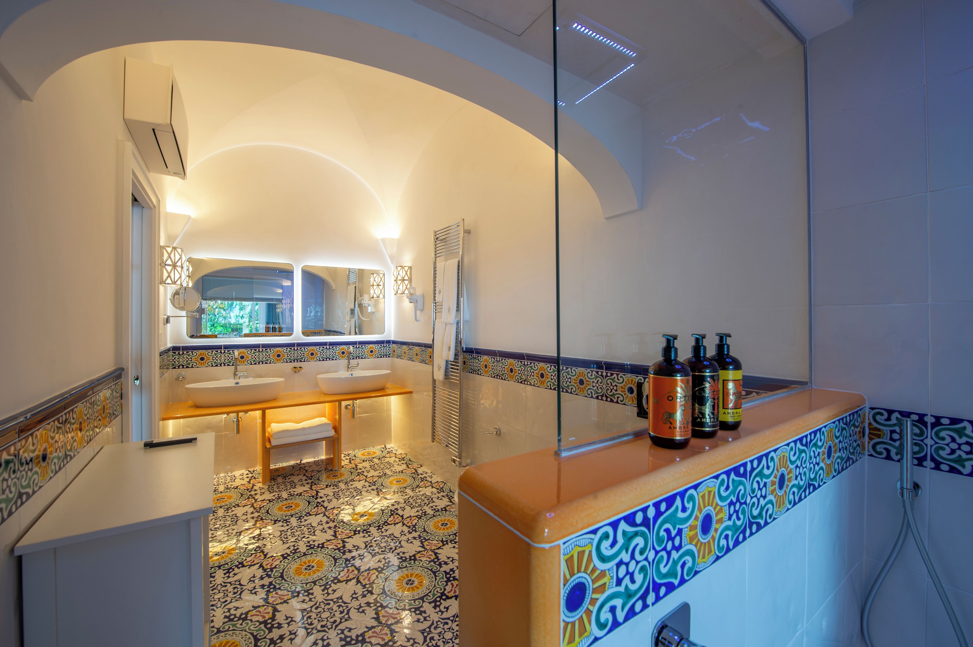 A bathroom with a white sink, a mirror, and a shower. There are three bottles on the counter.