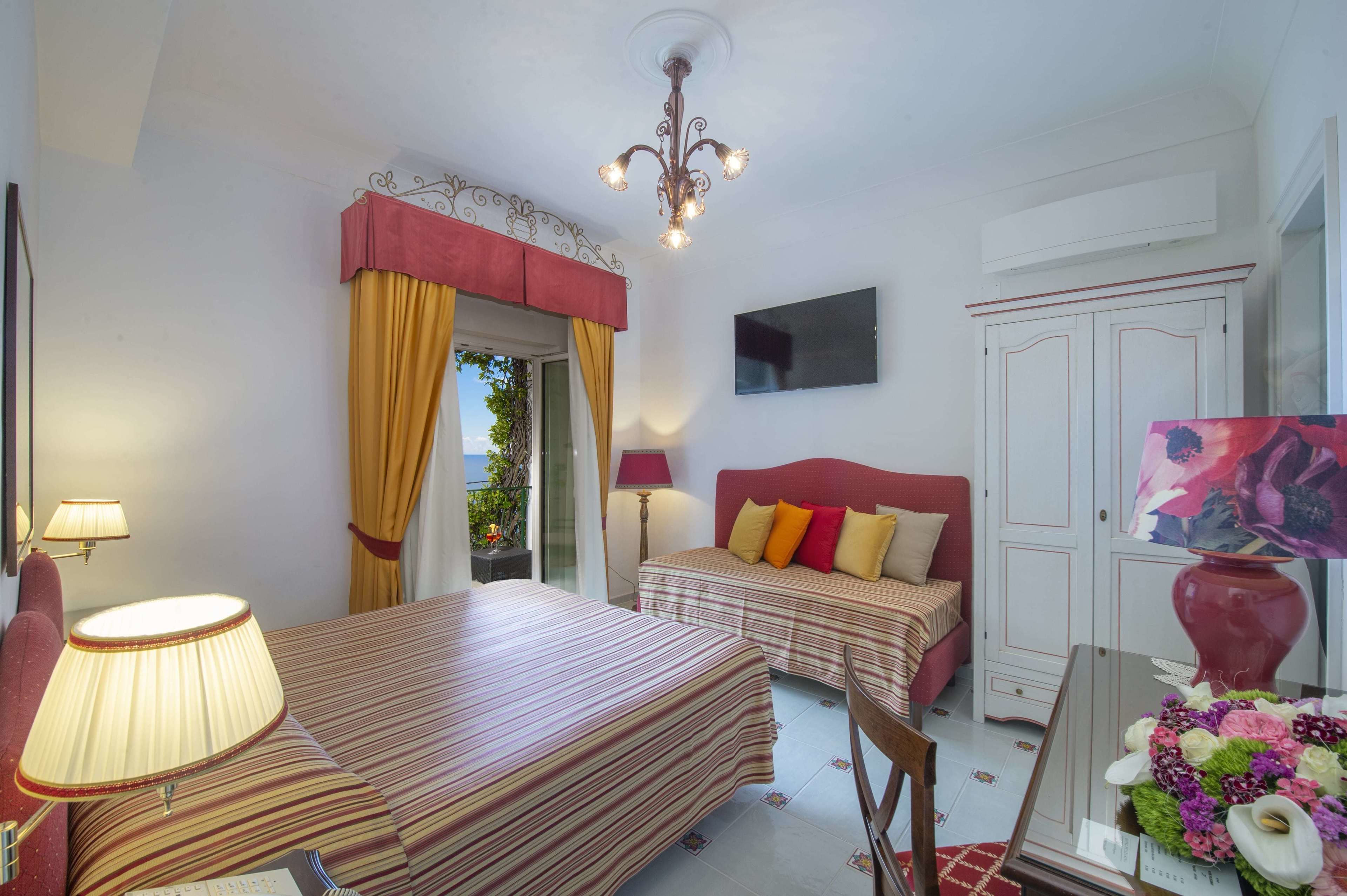 Habitación de hotel con cama, mesita de noche, lámpara y vistas al exterior.