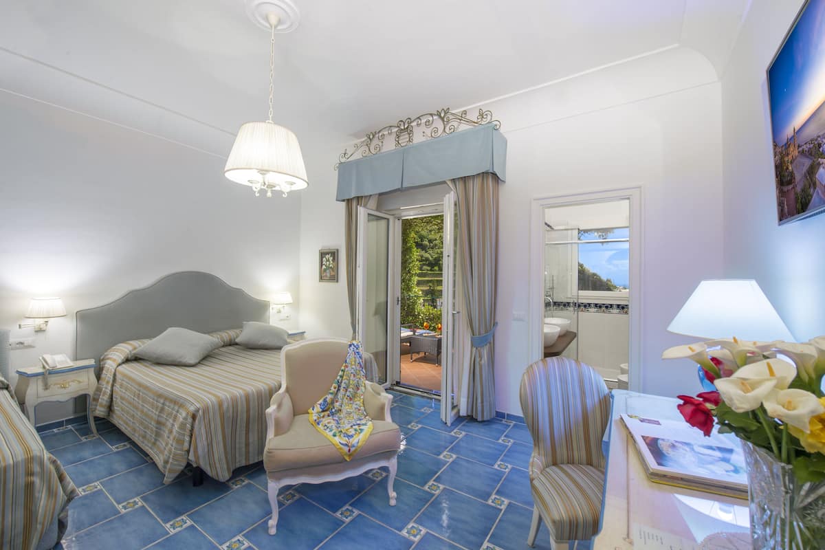 A hotel room with two beds, a chair, a table with a lamp, and a view of the outdoors.