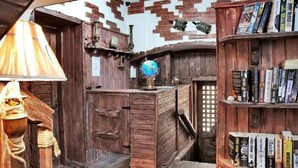 Habitació rústica amb parets de fusta, un globus terràqui, una biblioteca i una làmpada.