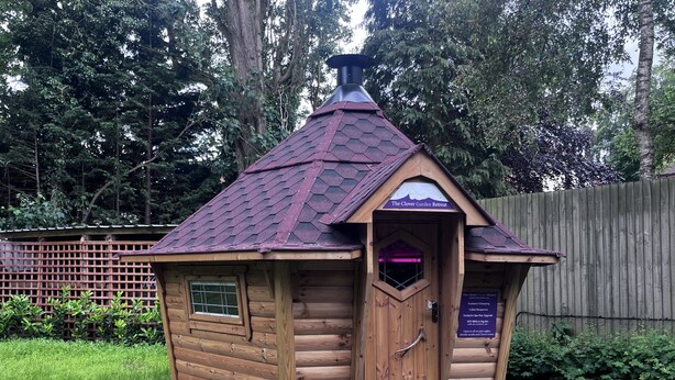A wooden cabin with a hexagonal roof, a small window, and a door with a sign. - Clover Spa and Hotel (Birmingham)