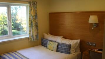 A neatly made bed with striped bedding, a wooden headboard, a bedside lamp, and a window with curtains.