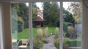 A room with a large window overlooking a garden with a gazebo, a lawn, and potted plants. - Clover Spa and Hotel (Birmingham)