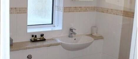 A bathroom with a sink, mirror, window, and tiled walls.