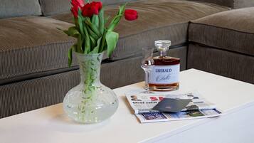 Uma mesa branca com um vaso de vidro contendo tulipas vermelhas, uma garrafa de L'HERAU e um jornal.