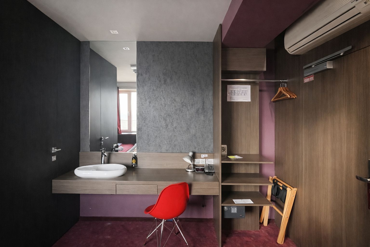 A modern bathroom with a vanity, sink, mirror, and red chair.