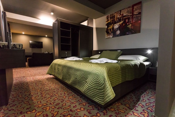 Una habitación de hotel moderna con una cama grande, un televisor de pantalla plana, un vestidor espacioso y un cuadro de paisaje urbano en la pared.