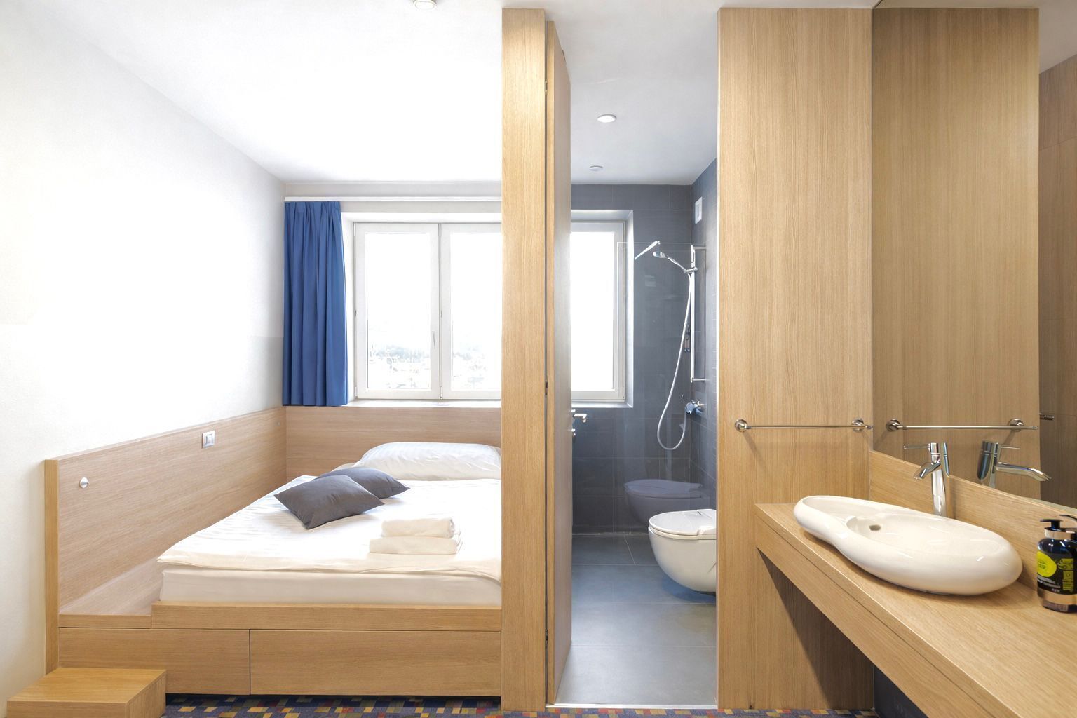 A modern hotel room with a wooden bed, a bathroom with a shower, and a sink.