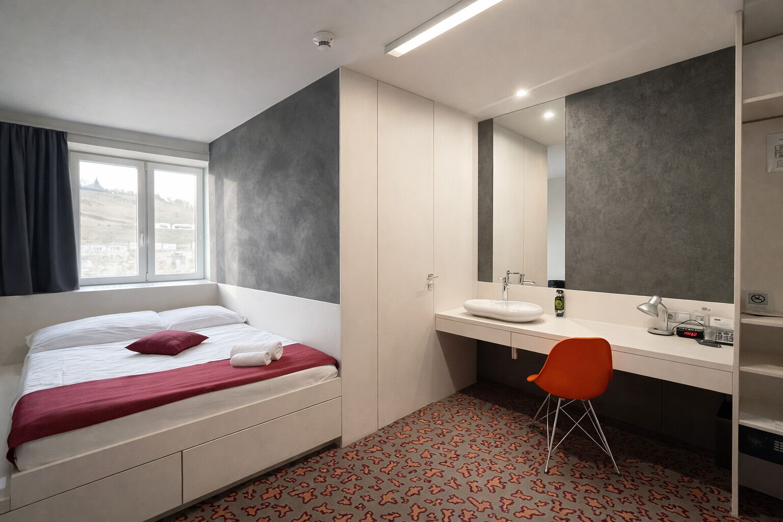 A hotel room with a bed, a desk with a mirror, a sink, and a chair.