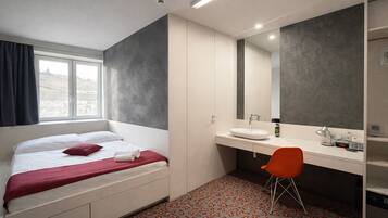 A hotel room with a bed, a desk with a mirror, a sink, and a chair.