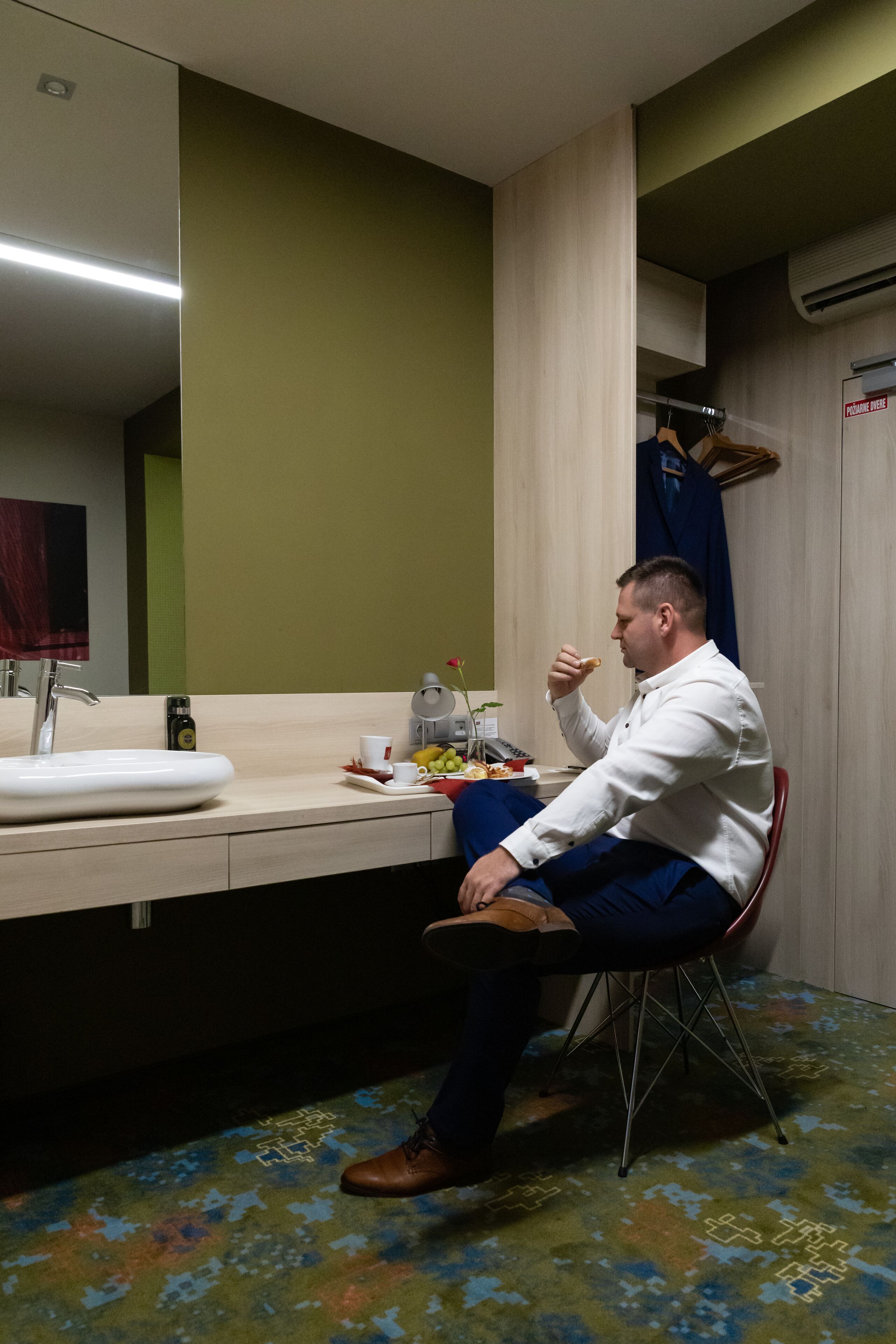 A man sitting at a table in a hotel bathroom, eating a snack.