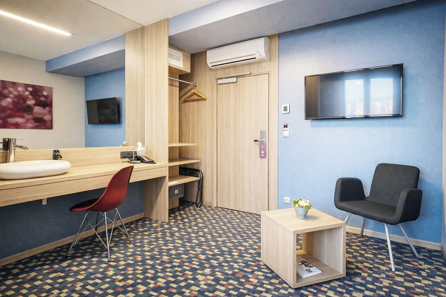 A hotel room with a wooden vanity, a red chair, a small table with a vase, a black chair, a TV, and a patterned carpet.