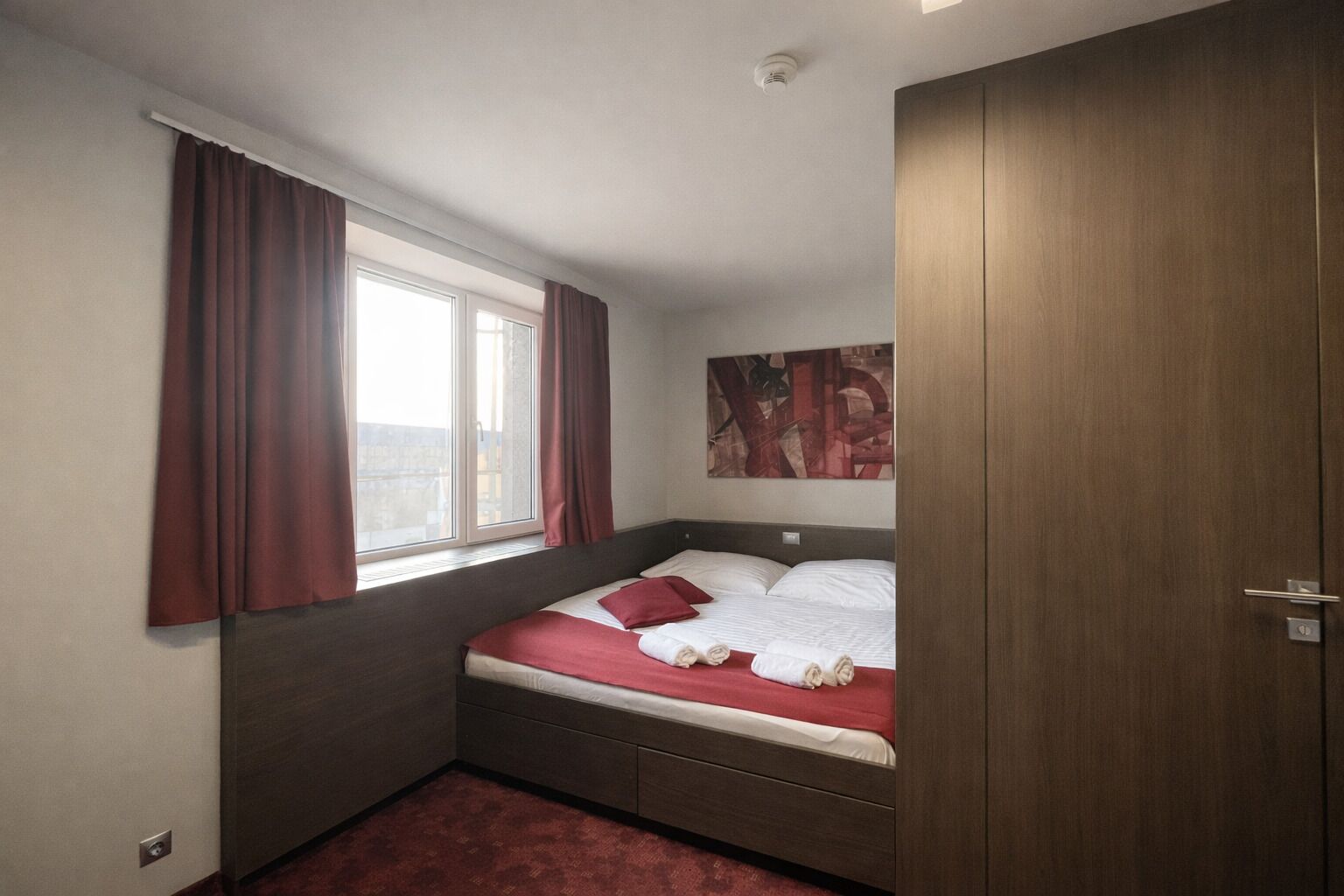 Un dormitorio con cama, una ventana con cortinas, un cuadro en la pared y un armario.