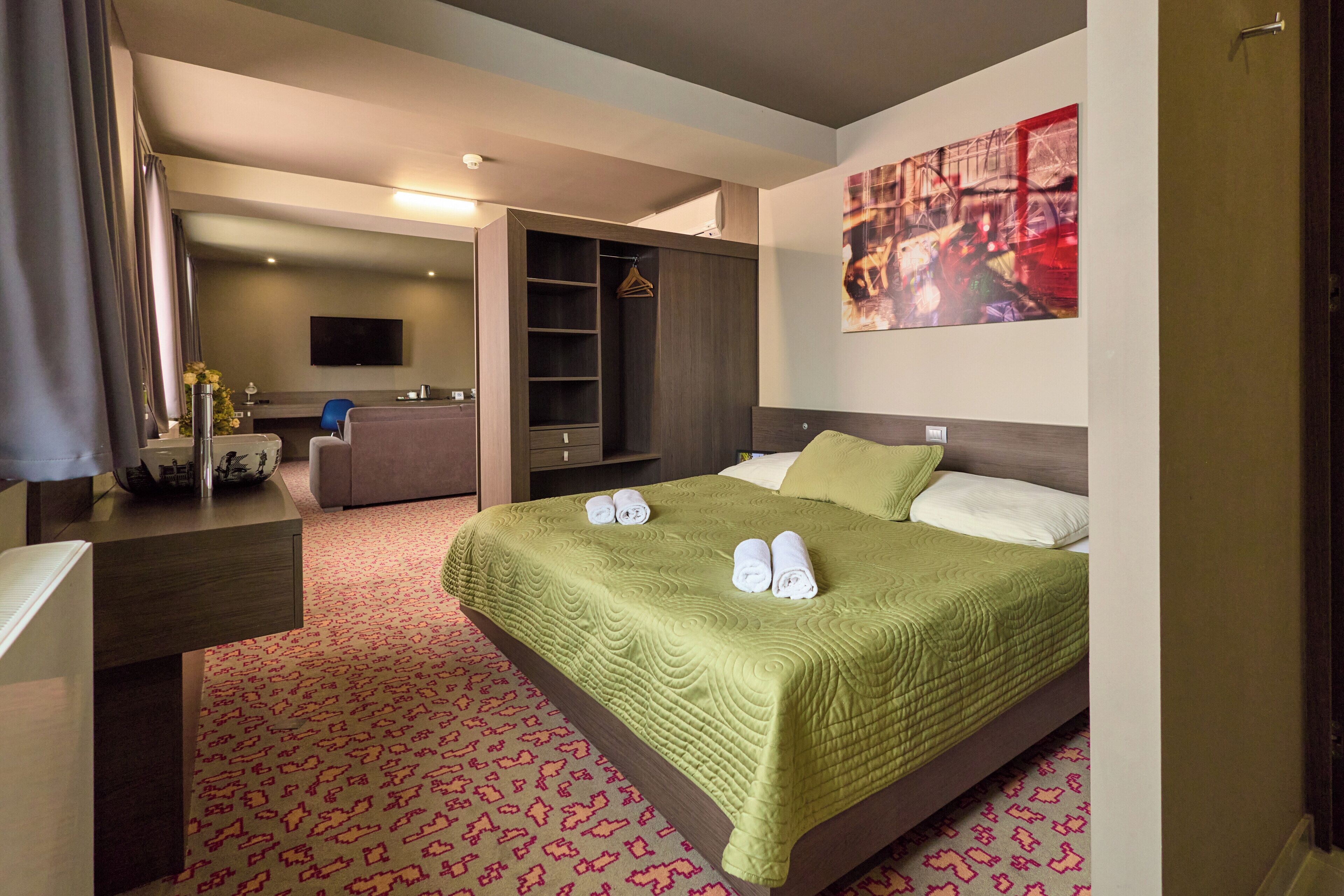 Une chambre d’hôtel équipée d’un lit, d’un bureau, d’une armoire et d’un téléviseur fixé au mur.