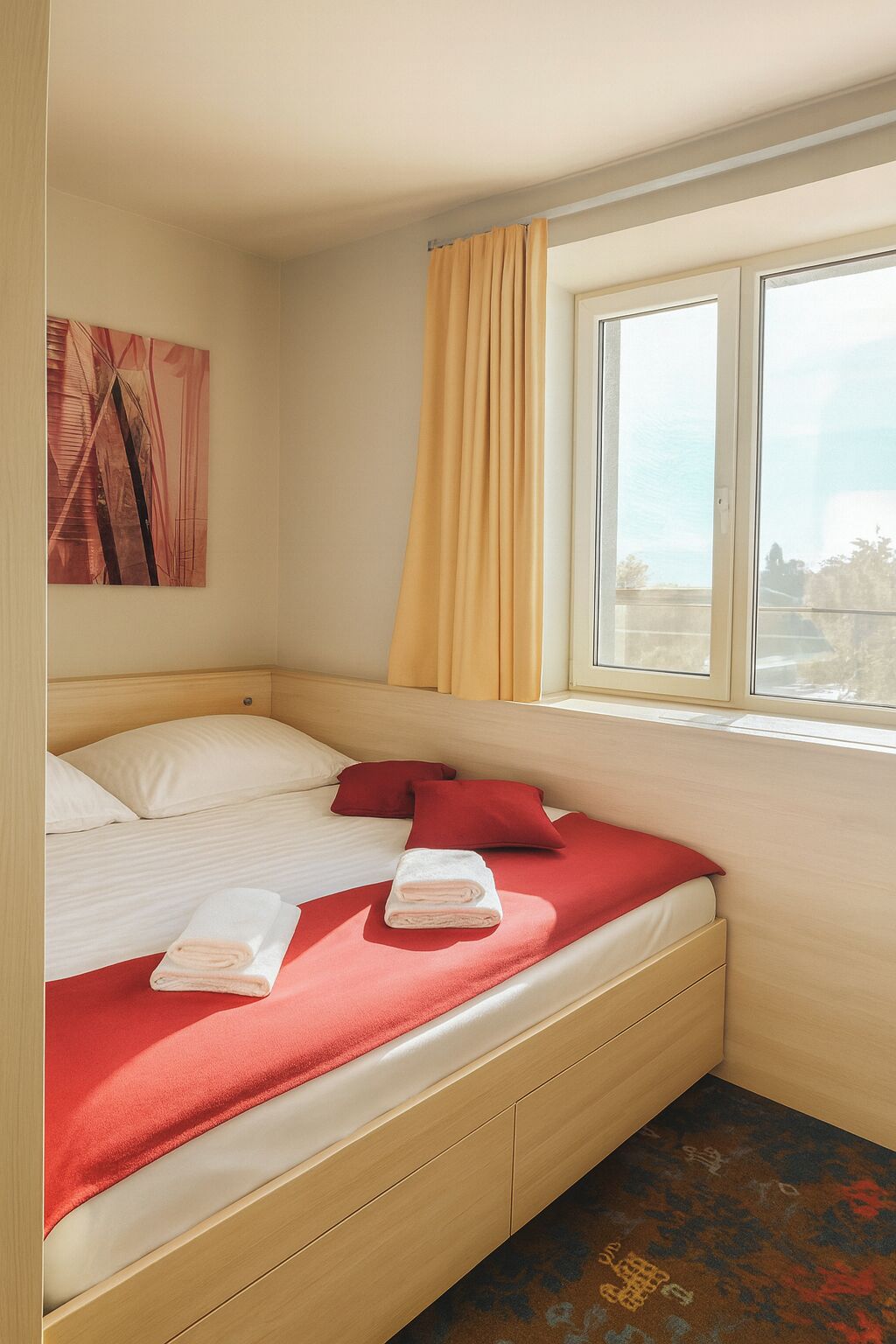 A hotel room with a bed, a window with curtains, a painting on the wall, and a carpet.