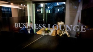 A business lounge with a glass partition and a table with a vase of flowers.