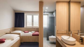 A hotel room with a bed, a bathroom with a sink and mirror, and a shower.