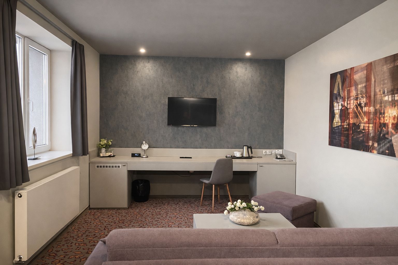 Een moderne hotelkamer met een flatscreen televisie, een bureau met stoel, een bank en een schilderij aan de muur.