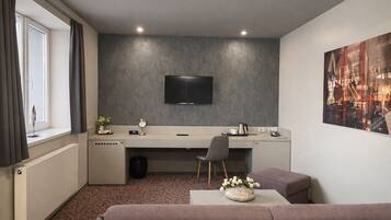 Een moderne hotelkamer met een flatscreen televisie, een bureau met stoel, een bank en een schilderij aan de muur.