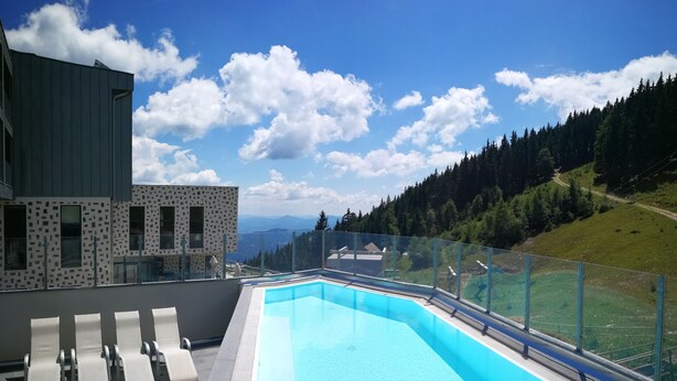 A rooftop pool with lounge chairs, a modern building with patterned facade, and a view of a forested hillside. - Wellness Hotel Montis (Mozirje)