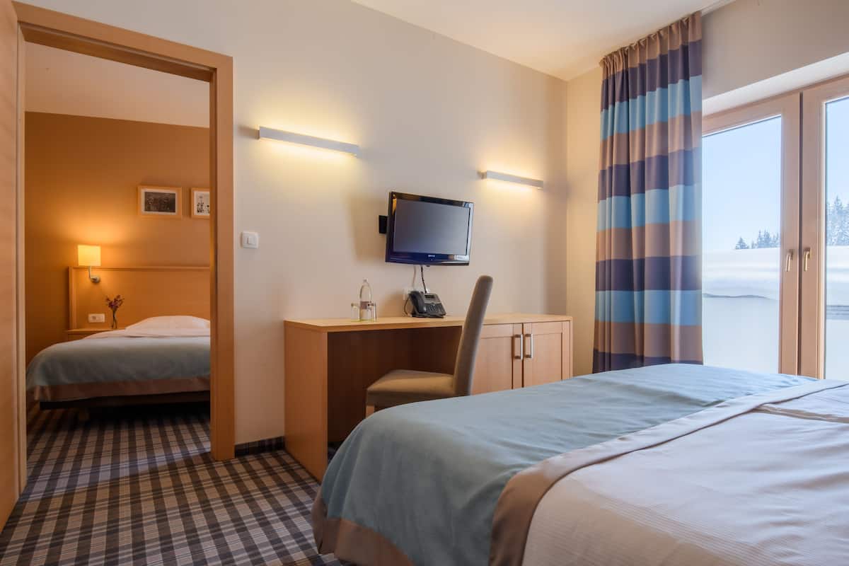 A hotel room with two beds, a desk with a computer, a TV, and a view of a snowy landscape.