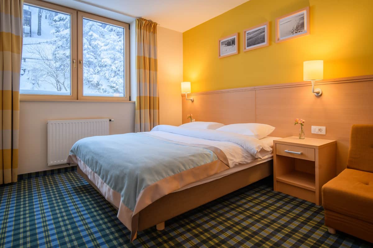 A hotel room with a bed, bedside table, chair, and a window with curtains.