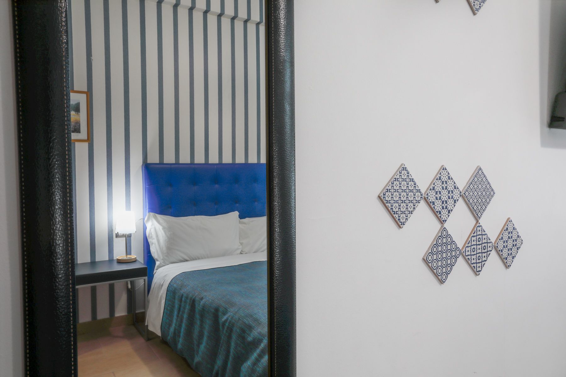 Een slaapkamer met een blauw hoofdeinde, een bed met wit beddengoed en een nachtkastje met een lamp.