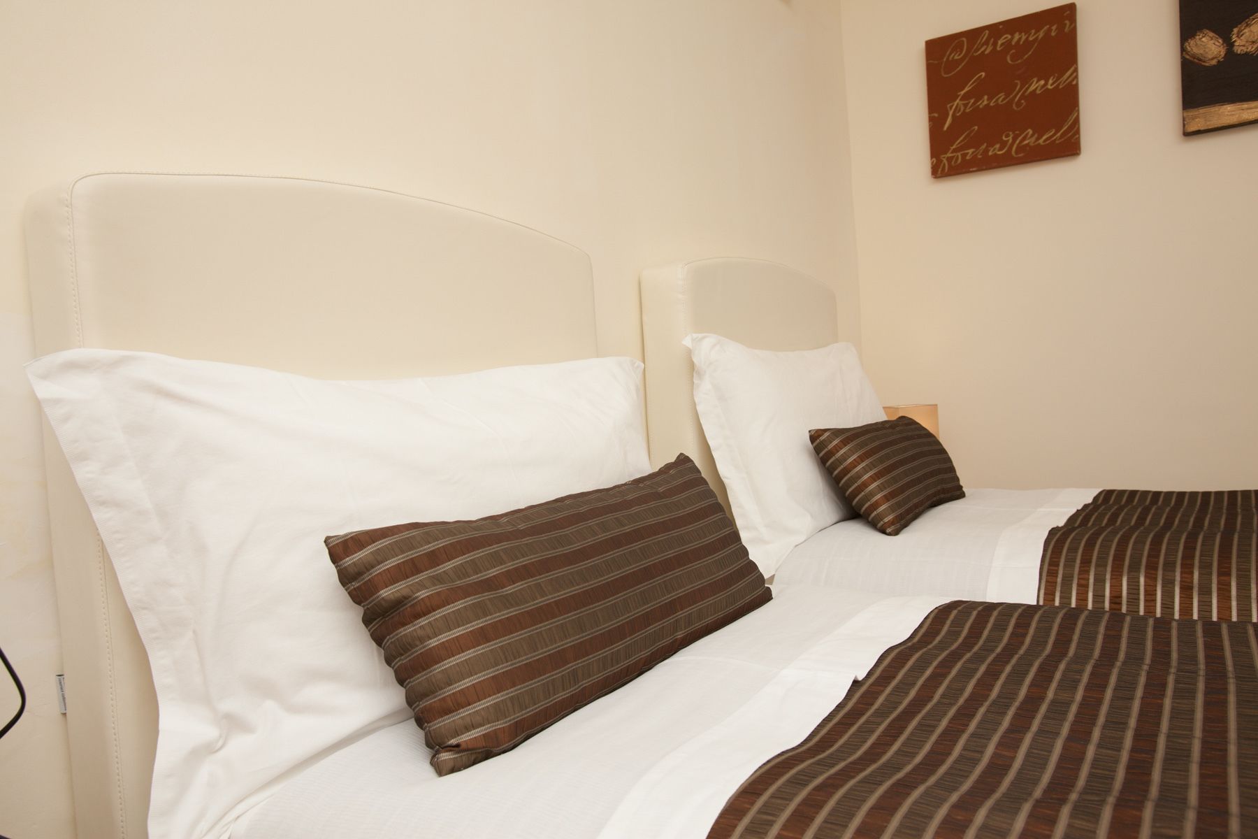 A double bed with white and striped brown bedding, a headboard, and a wall-mounted sign.