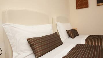 A double bed with white and striped brown bedding, a headboard, and a wall-mounted sign.