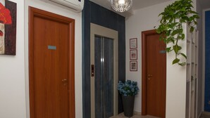 Un pasillo con puertas de madera, un ascensor central y una planta en maceta.